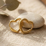 Gold heart-shaped earrings on a textured surface with a book and eucalyptus leaves.